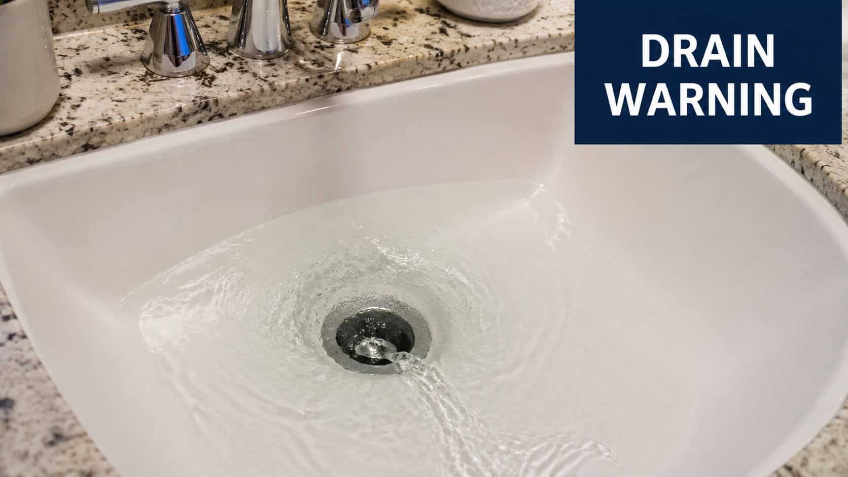 A close up view of a white bathroom sink filling with water, featuring a dark drain warning sign.