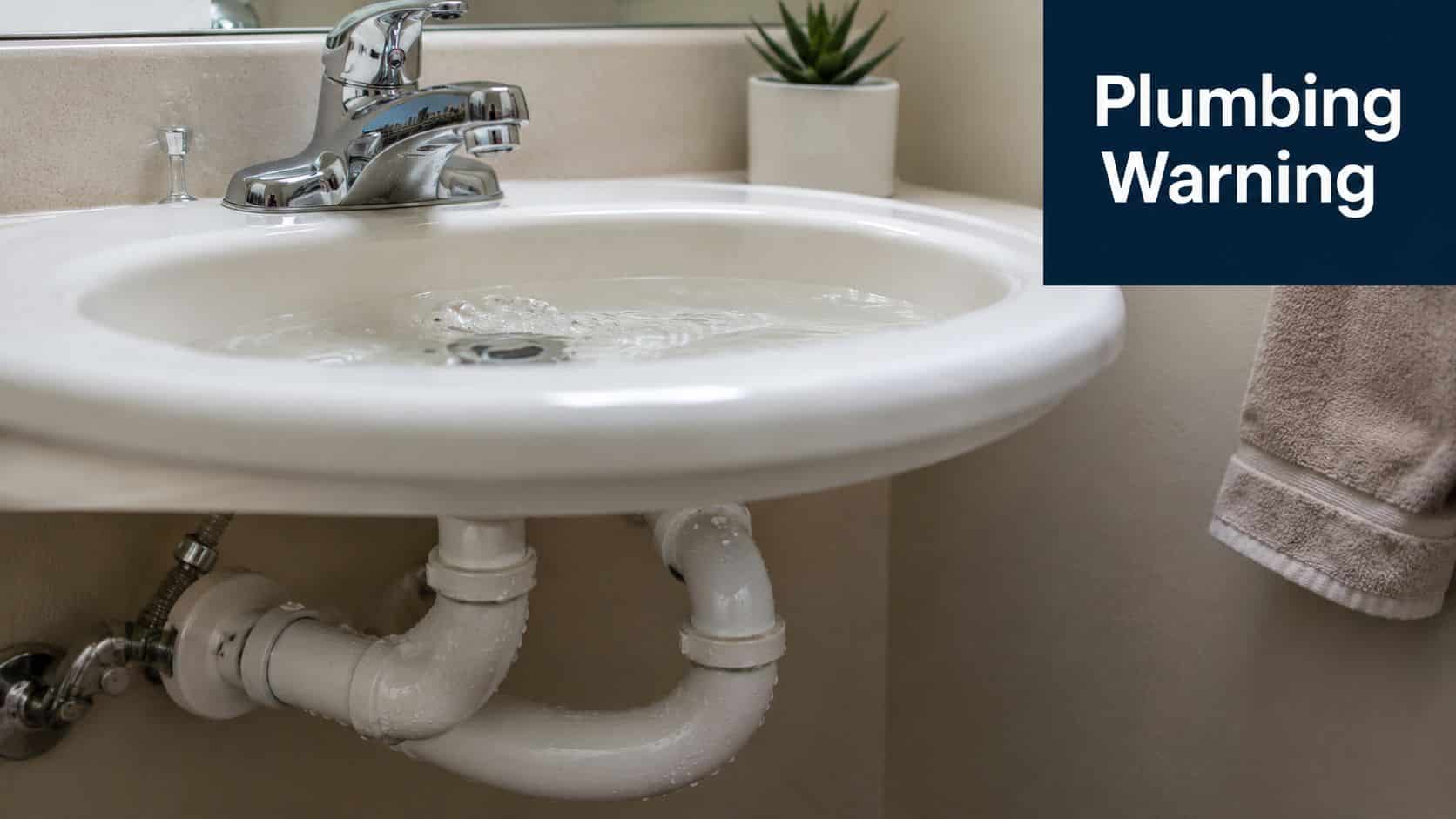 A bathroom sink filled with water with a leaking P-trap pipe underneath, signaling a plumbing emergency.